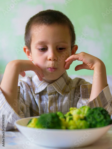 Fotografía Picky boy staring unhappily at bowl of green broccoli refusing to eat healthy ve