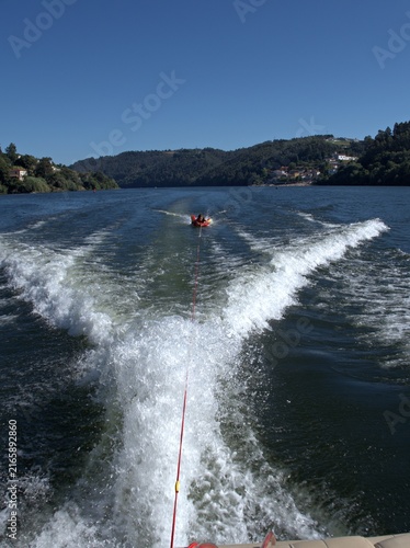 Canvastavla Wide V shaped wake and a red towable tube with a rider trailing behind a moving
