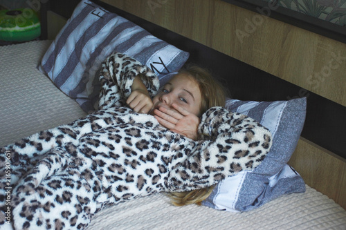 a girl in a terry robe lies on a pillow. the child smiles and looks away. the child woke up, lies relaxing and enjoys the new day