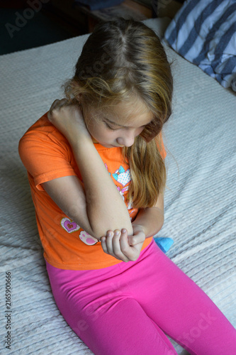 A beautiful young woman in casual clothing is holding her elbow. a pained expression is frozen on her face. Her gaze is filled with sadness caused by joint pain, an injury, or some other ailment.