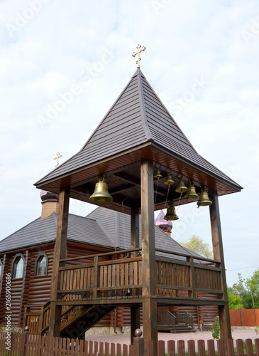 wooden tower with church bells and a cross on the background of the church. religion and culture. Orthodox Christianity. small regional temple