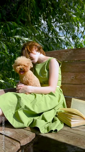girl petting a small dog on her lap. Young girl with small attentive dog, teenager sitting maltipoo on bench.