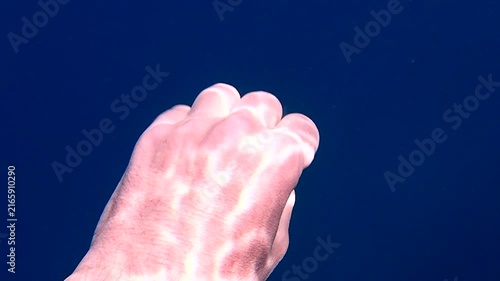 Underwater human hand making grabbing gestures with light ripple patterns on back