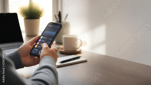 Professional individual managing personal finances on a smartphone at a minimalist home office desk with a clean financial dashboard interface