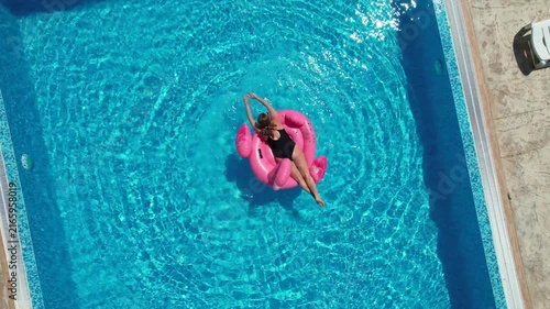 Aerial drone view of beautiful woman on flamingo pool float in pool. Summer holidays
