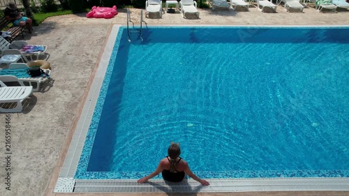 woman sitting on the edge of the pool in hotel from above view, aerial top view from drone, summer relaxation in hotel
