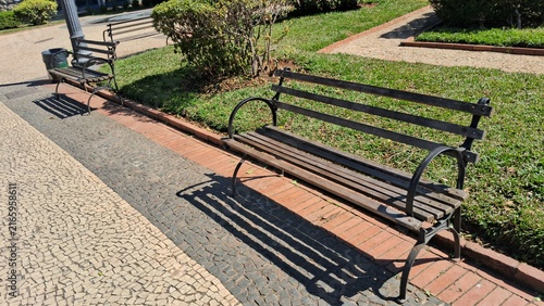 Obraz na plátně Empty wooden park benches sitting on a sunny stone paved pathway