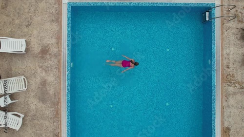 Drone view from above of young woman swimming in turquoise pool water in hotel. Summer holidays, enjoying summer vacations. Aerial top view from drone. Beach vacation
