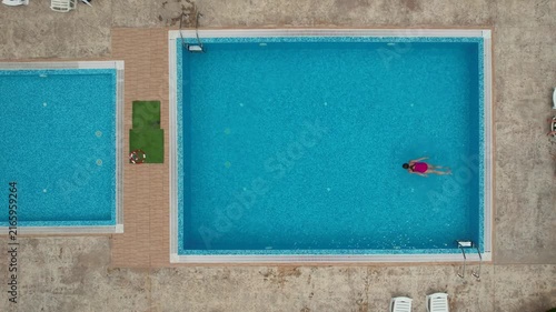 Drone view from above of young woman swimming in turquoise pool water in hotel. Summer holidays, enjoying summer vacations. Aerial top view from drone. Beach vacation
