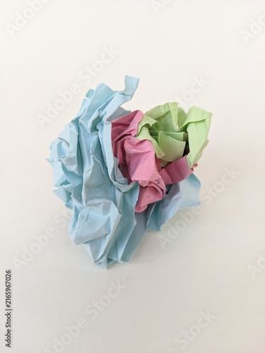 Crumpled colorful paper ball symbolizing creativity, recycling and discarded ideas on plain white background.