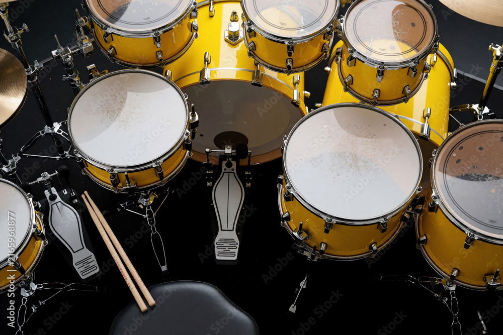 Obraz premium Overhead view of bright yellow drum kit on dark stage floor. Professional percussion set includes snare, tom, bass drum with pedals, sticks. Musician equipment prepared for rock concert, band