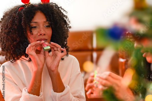Fotografie A cheerful Black woman and her Latina best friend raise noisemakers and blow har