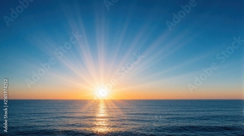 Sunrise breaks over tranquil ocean, casting golden rays across calm blue waters. Vibrant horizon blends soft orange, pink hues with expansive clear sky above. Horizon meets undisturbed sea, dawn