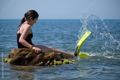 Canvas Print Girl sitting on a rock in the sea with flippers