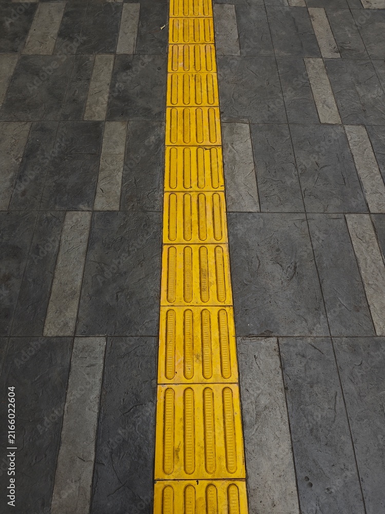 Fototapeta premium Yellow tactile paving blocks for visually impaired navigation on pedestrian sidewalk