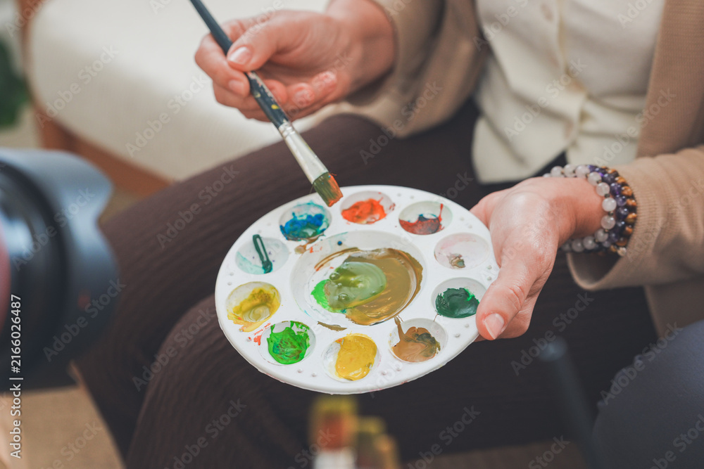 Obraz premium Paint brushes in a jar with freshly mixed watercolours by a bright window at home.