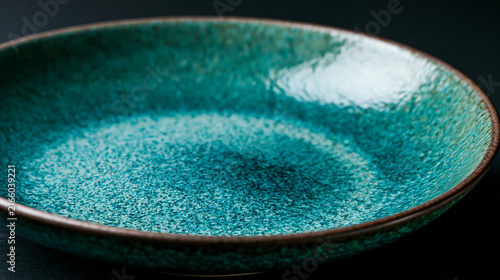 Empty turquoise ceramic plate with textured glaze against a dark background