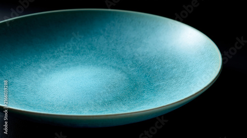 Empty shallow turquoise ceramic bowl with textured surface on dark background