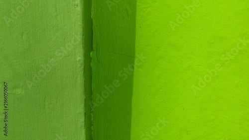 Close-up of a bright green painted wall corner, showing vibrant color, smooth texture, and subtle shadow lines. Concept of modern minimalist interior design and abstract architectural background.