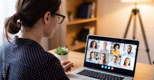 Businesswoman participating in video conference call on laptop screen with diverse team colleagues during remote work from home in modern bright comfortable office interior setting