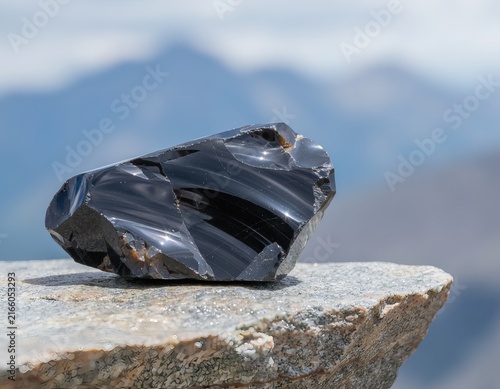 Obsidian Stone Balancing on a Rock Edge at a Mountain Summit with Hazy Peaks Behind