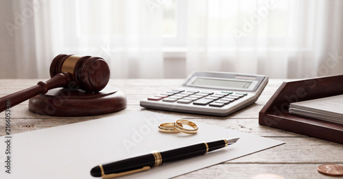Divorce settlement papers with two golden wedding rings resting on a wooden office desk next to a wooden judge gavel and calculator for legal proceedings