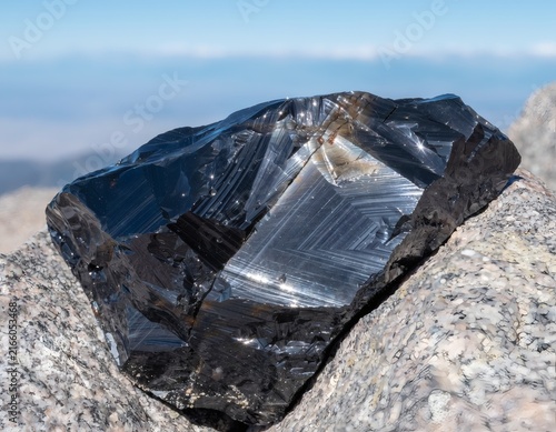 Obsidian Stone with Striped Glassy Patterns Fitting Snugly Between Summit Rocks Against Blue Sky and Peaks