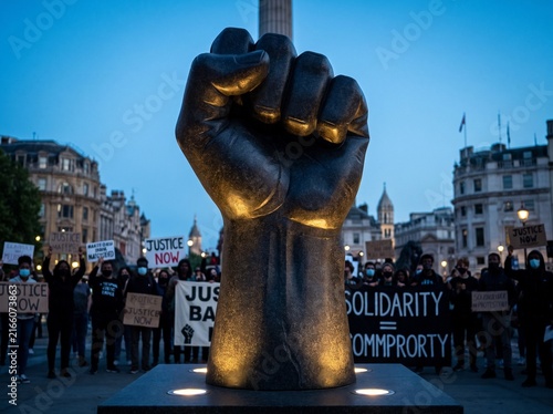Large Bronze Fist Sculpture at Night in Public Square with Crowd Holding Signs for Justice and Solidarity