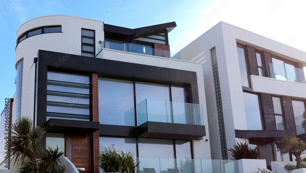 Fototapeta premium Modern luxury residential building with large glass windows and rooftop terrace under clear sky