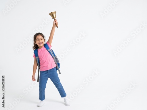 Happy little schoolgirl holding a golden bell up high, celebrating the start of school.