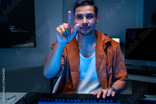 Foto A dark-haired network defence analyst pauses in thought at his desk at a multi-monitor workstation in a darkened control room, protecting corporate networks from hackers and data breaches