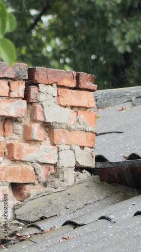 Close-up vertical video of raindrops pouring over an aged weathered brick chimney on a slate roof.