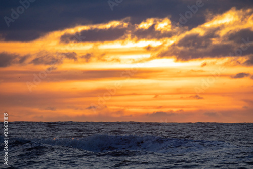 A stunning sunset with vibrant colors reflecting on ocean waves, framed by dramatic clouds, creating enchantment