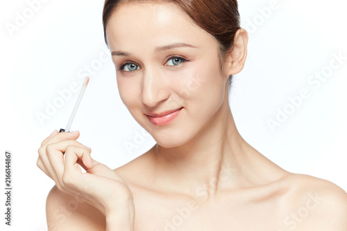 Konstfotografi Smiling young woman holding lip gloss applicator with natural makeup
