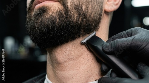 Close-up of a barber using an electric trimmer to style a man's beard, showcasing grooming and personal care services