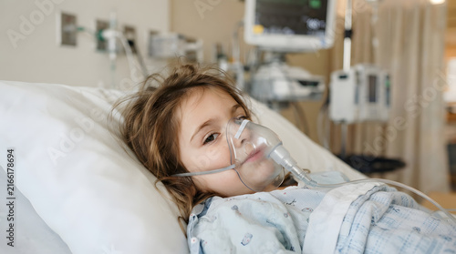 Young child wearing an oxygen mask lying in a hospital bed for medical treatment