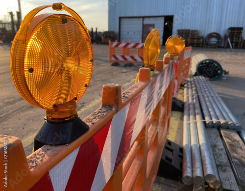 Sunlit amber safety lights mounted on textured barricades with reflective tape in an industrial environment.