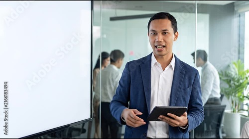 Busy young Indonesian business man executive standing in office using digital tablet. Young professional businessman corporate manager wearing suit and glasses holding tab working on finance project