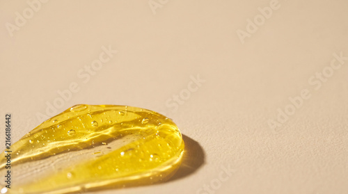Close-up texture of golden serum or gel with small bubbles and highlights, casting a soft shadow on a neutral beige background, cosmetic product sample, skincare