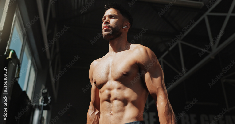 Fototapeta premium Fitness, gym and bodybuilder man with music and thinking of training, muscle growth and self care. Earphones, workout playlist and person or health club membership for exercise, strong and wellness