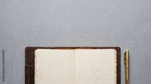 Opened vintage leather bound notebook with blank aged pages, next to a golden pen, flat lay on a textured gray surface, top down view, ideal for journaling or note-taking concepts