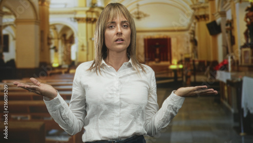 Foto Woman raising hands and palms near ears while looking upward inside a building nave with pews and altar visible; prayerful contemplation