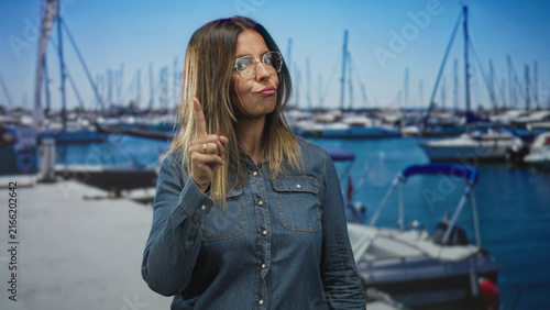Foto Woman points finger to camera with pursed lips, glasses and denim shirt, ring on finger in studio marina backdrop; warning confidence