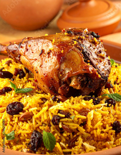 A close up of whole roasted lamb on a bed of spiced mandi rice with raisins and nuts.