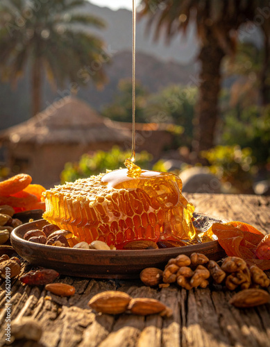 Yemeni honey drizzled over a piece of honeycomb on a wooden plate with nuts and dried fruits.