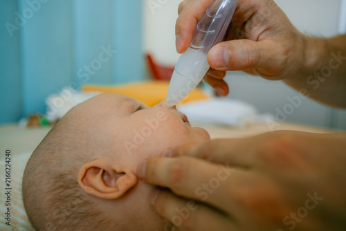 фотографія Father holding an infant on a changing table, using a nasal aspirator to clean t