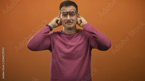 Obraz na plátně Young hispanic man with moustache wearing magenta long sleeve shirt holds round glasses to face and smiles facing camera in studio; playful charm