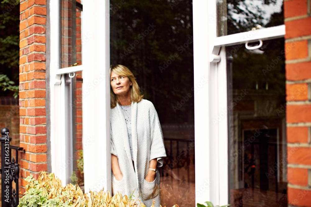 Fototapeta premium Morning, thinking and mature woman by door of home for break, relax or vision and wellness. Daydream, idea and reflection of person on terrace of apartment for memories, nostalgia or planning
