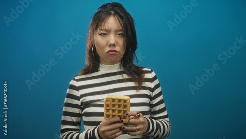 Fotografie Woman holding waffle with both hands, lips pursed in disgust while wearing striped top in studio; disgust hesitation