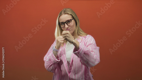 Fotografie Woman with fists raised and punching gesture in studio with orange backdrop and pink striped shirt; playful confidence